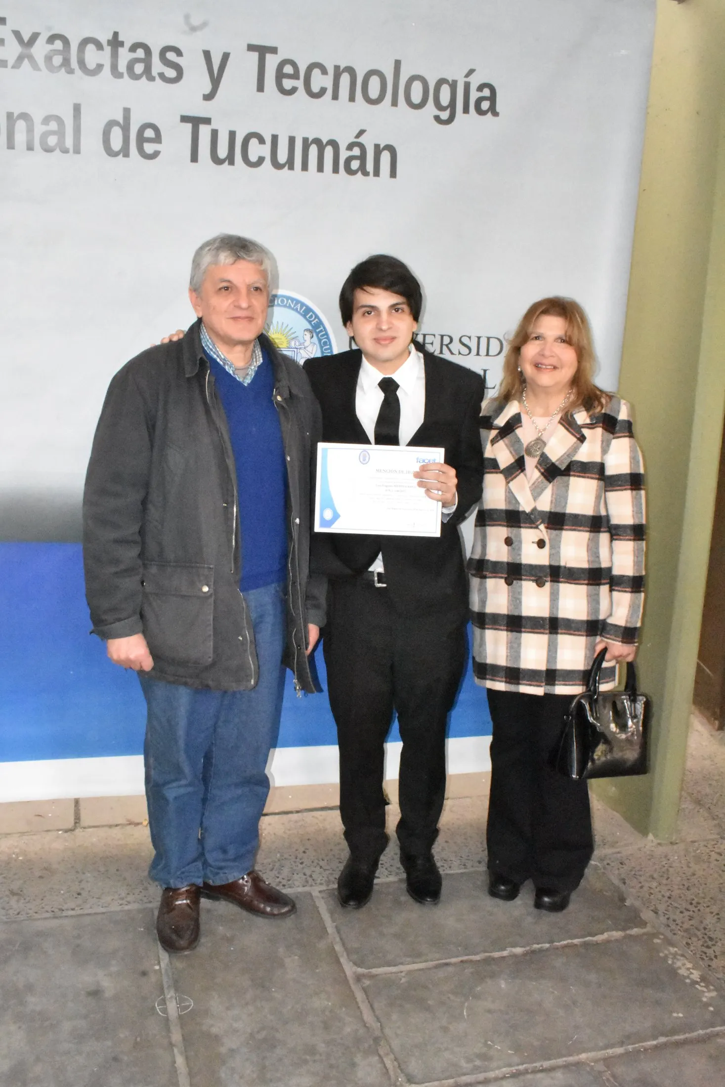 Luis Medina Raed avec sa famille, tenant la Mention d'honneur, devant la banderole de la Faculté des Sciences Exactes et Technologie (UNT).