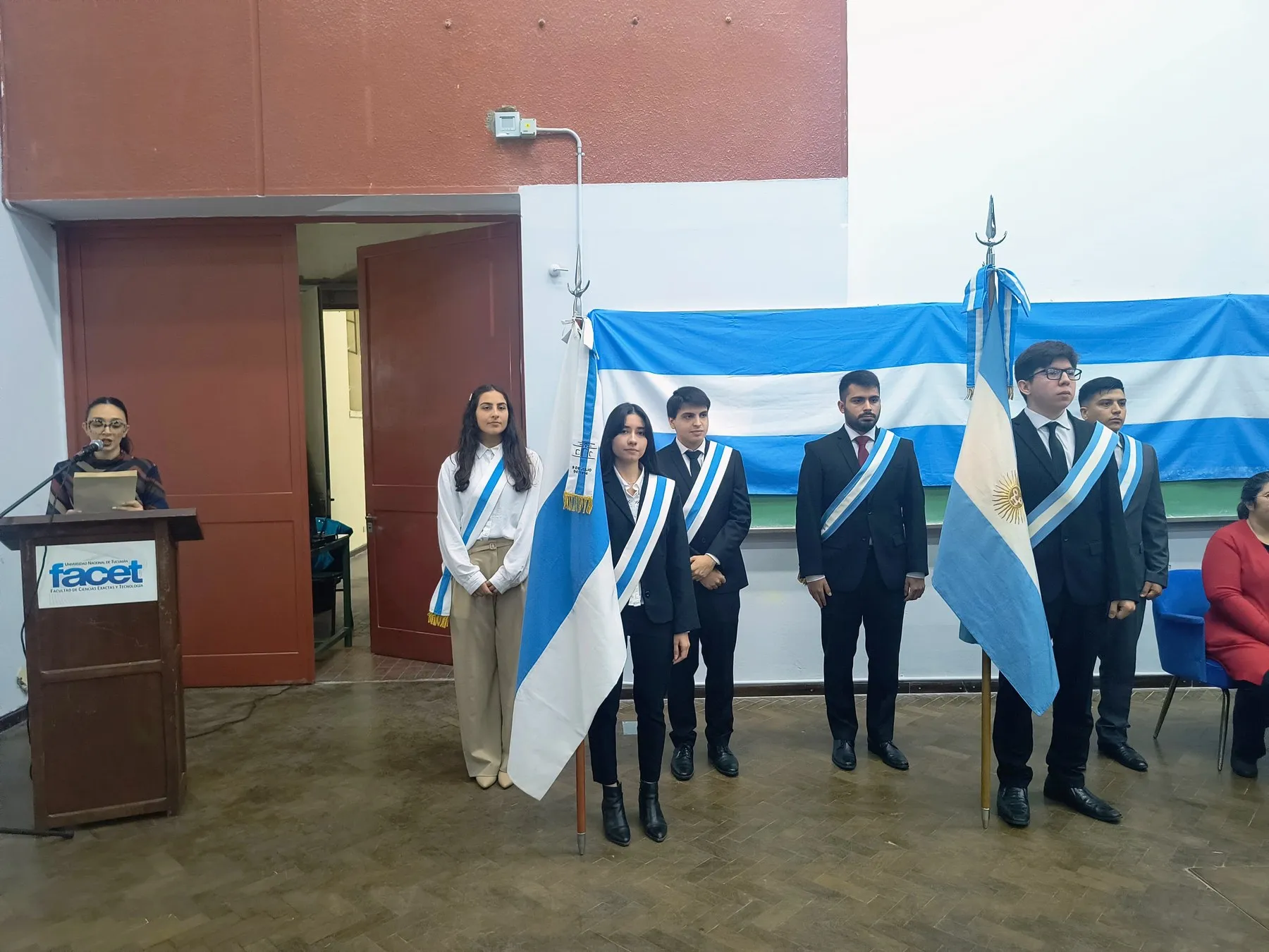 Les porte-drapeaux et les escortes en formation avec les drapeaux lors de la cérémonie de la FACET, avec une autorité lisant au pupitre.