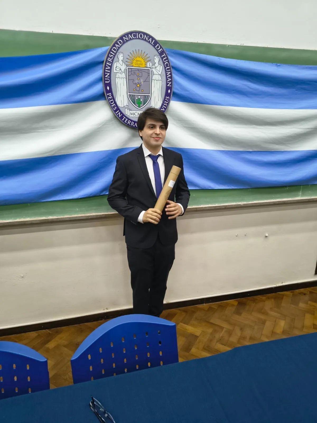 Luis Medina Raed con su diploma frente a la bandera de la Universidad Nacional de Tucumán.